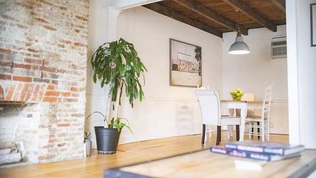 A dining area with a brick wall, a potted plant, a table with chairs, and a hanging light fixture. - The Rodney House (Lewes)