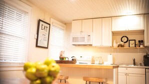 A kitchen with white cabinets, a microwave, and a framed 'EAT' sign on the wall. - The Rodney House (Lewes)