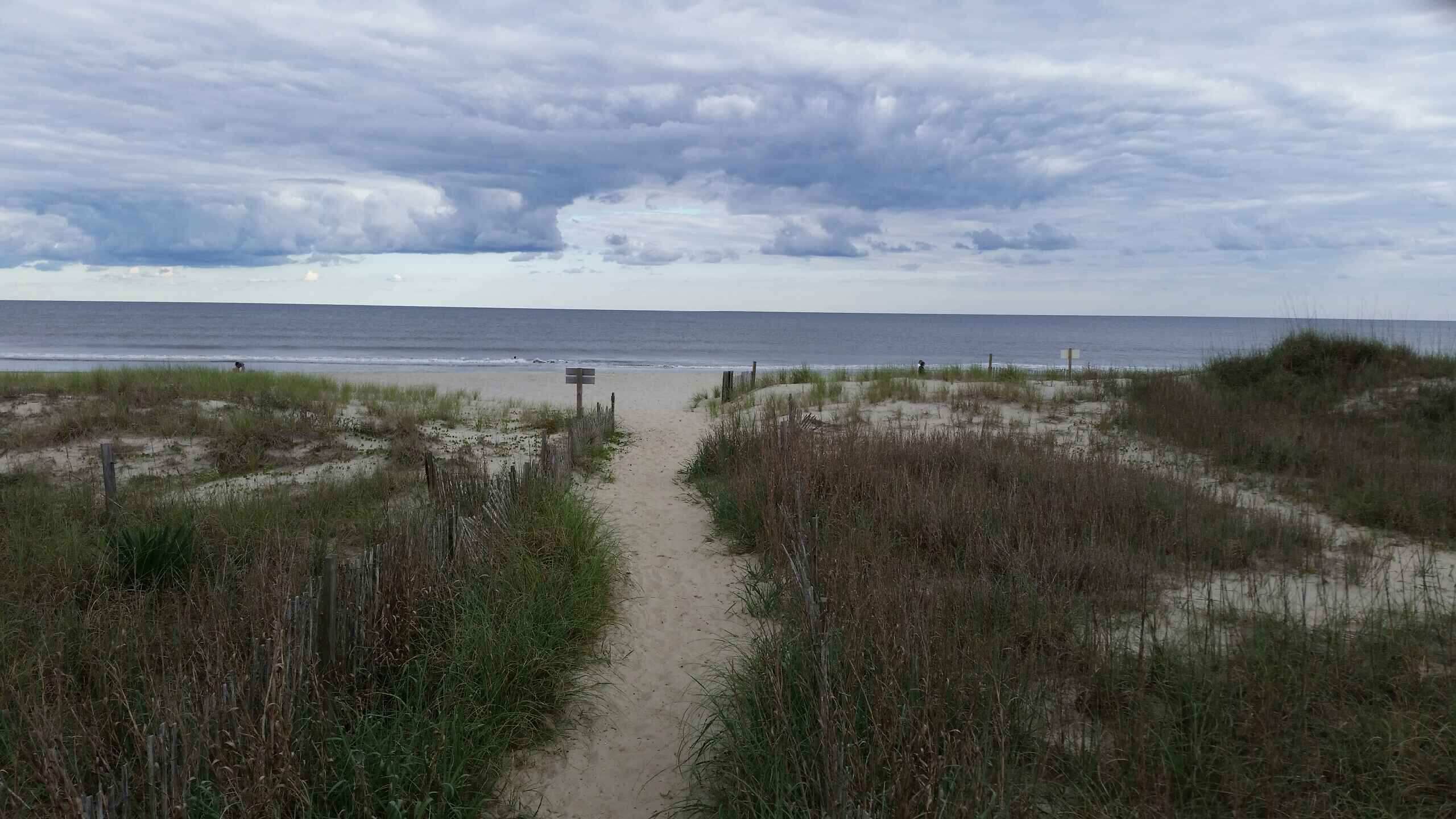 Um caminho de areia que leva a uma praia, com dunas gramadas de cada lado.