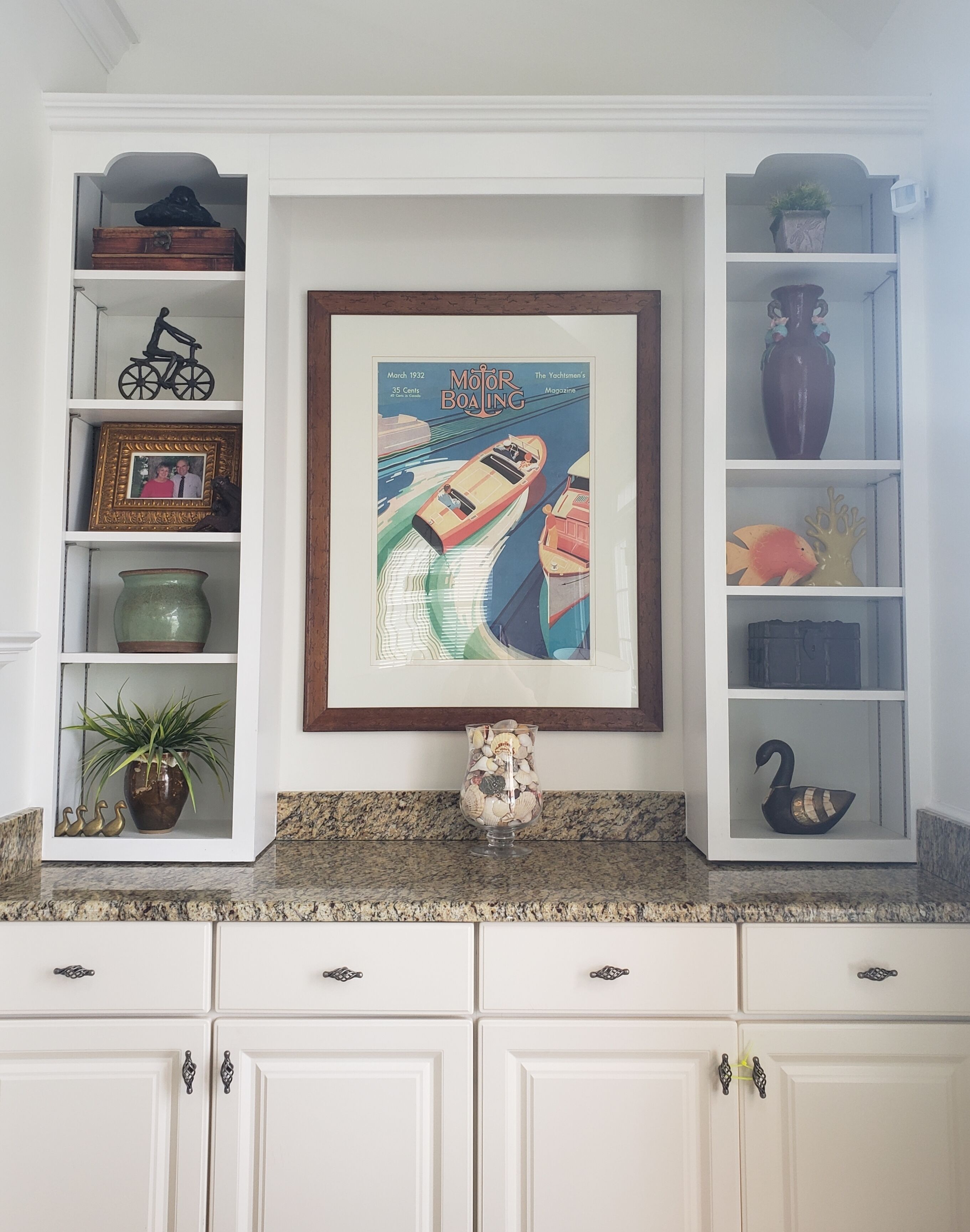 A kitchen with white cabinetry, a granite countertop, and a framed magazine cover on the wall.