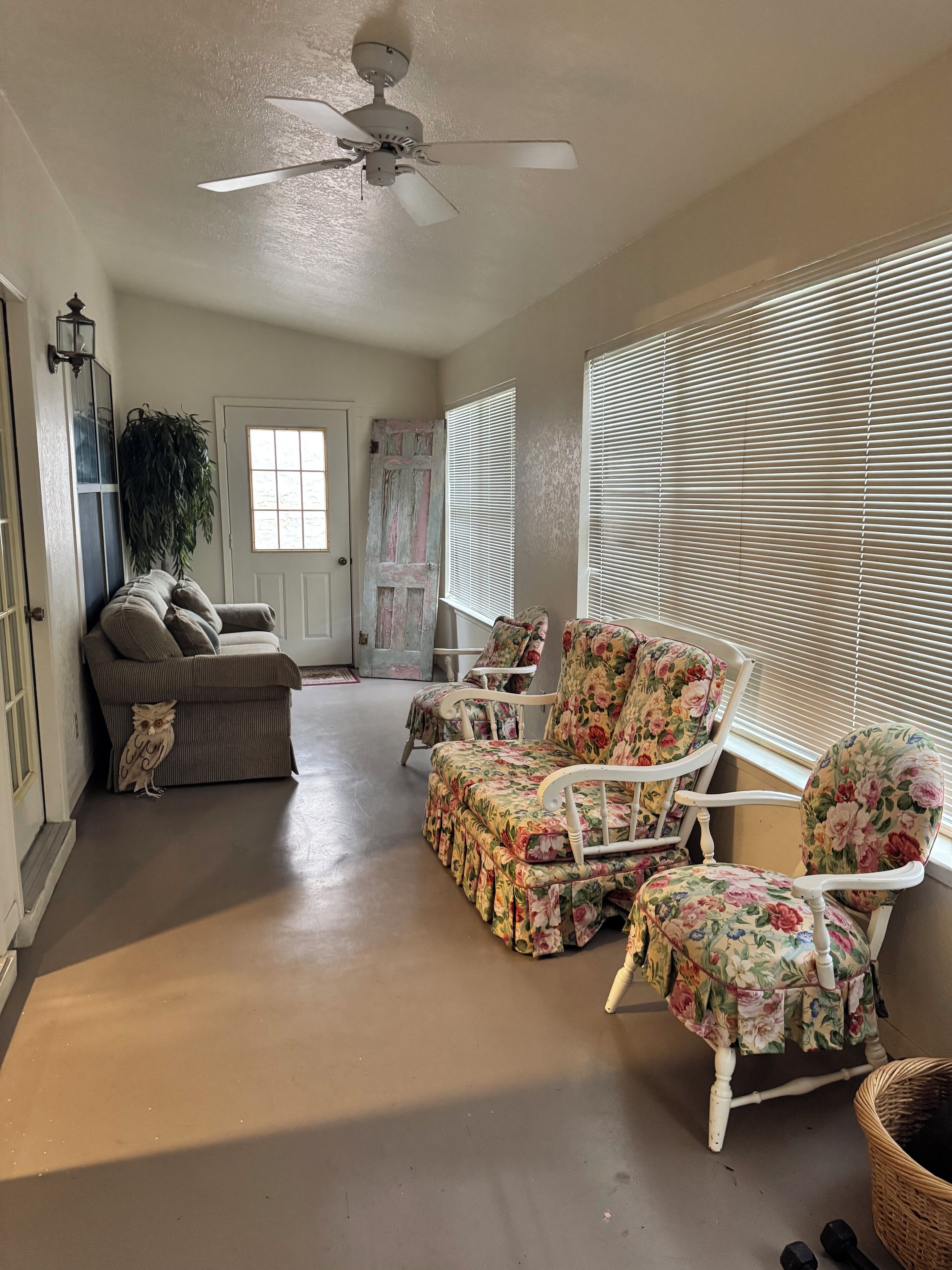 A spacious room with a ceiling fan, a floral-patterned chair, a sofa, and a door with a window.