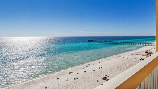 Una playa con un muelle que se adentra en el océano, arena dorada y un cielo azul despejado.