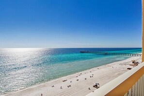 Una playa con un muelle que se adentra en el océano, arena dorada y un cielo azul despejado.