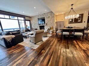 Un vaste salon agrémenté d’une cheminée en pierre, un coin repas avec un lustre et une grande fenêtre offrant une vue imprenable.