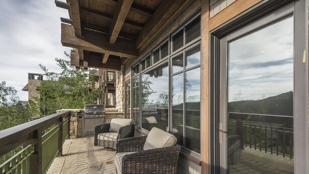 Eine überdachte Terrasse im Freien mit Korbmöbeln, einem Grill und Blick auf die umliegende Landschaft.
