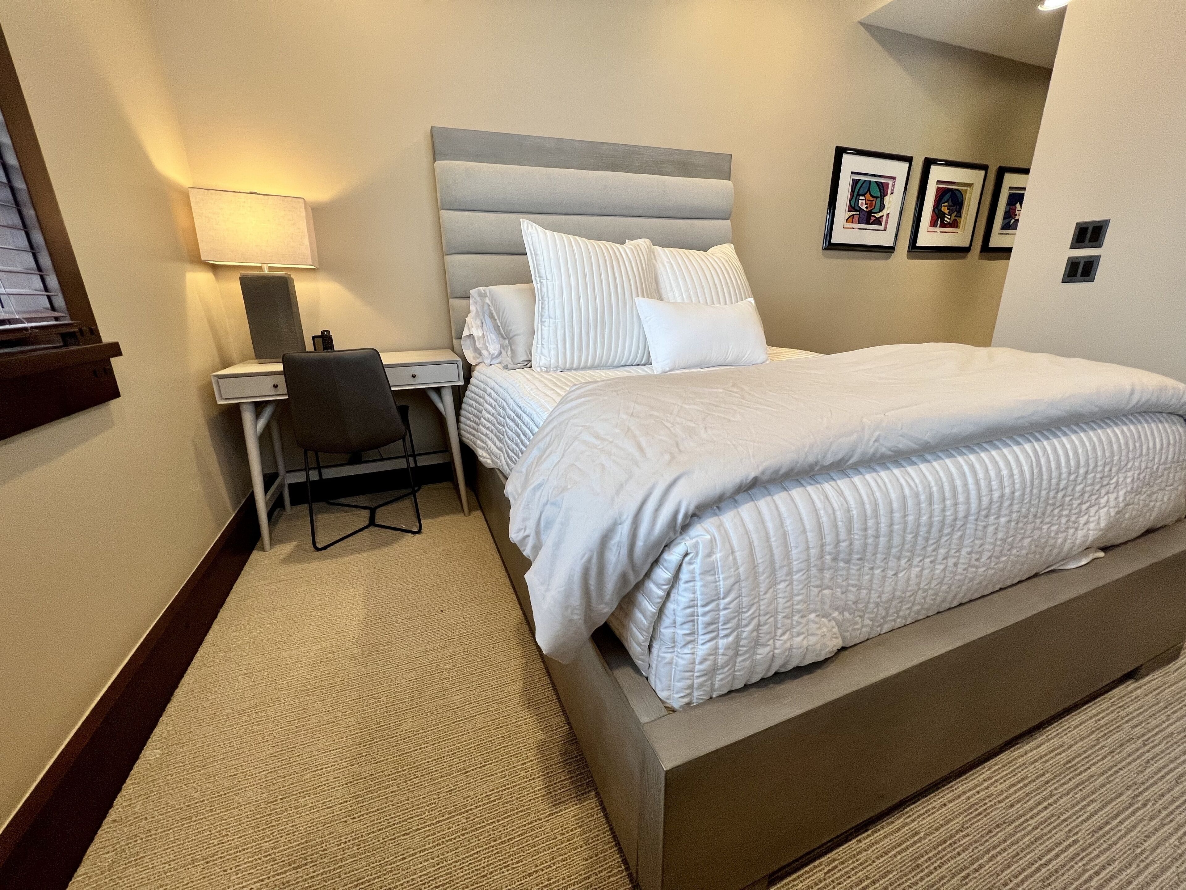Ein Hotelzimmer mit Bett, Schreibtisch, Stuhl, Lampe und gerahmten Bildern an der Wand.