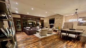 Ein geräumiges Wohnzimmer mit Kamin, Holzboden und einem Essbereich mit Tisch und Stühlen.