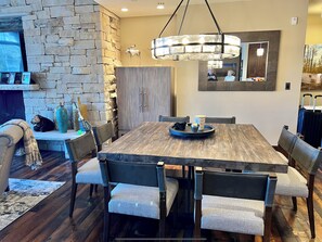 Un espace repas comprenant une grande table en bois, des chaises rembourrées, un mur en pierre et une cheminée.