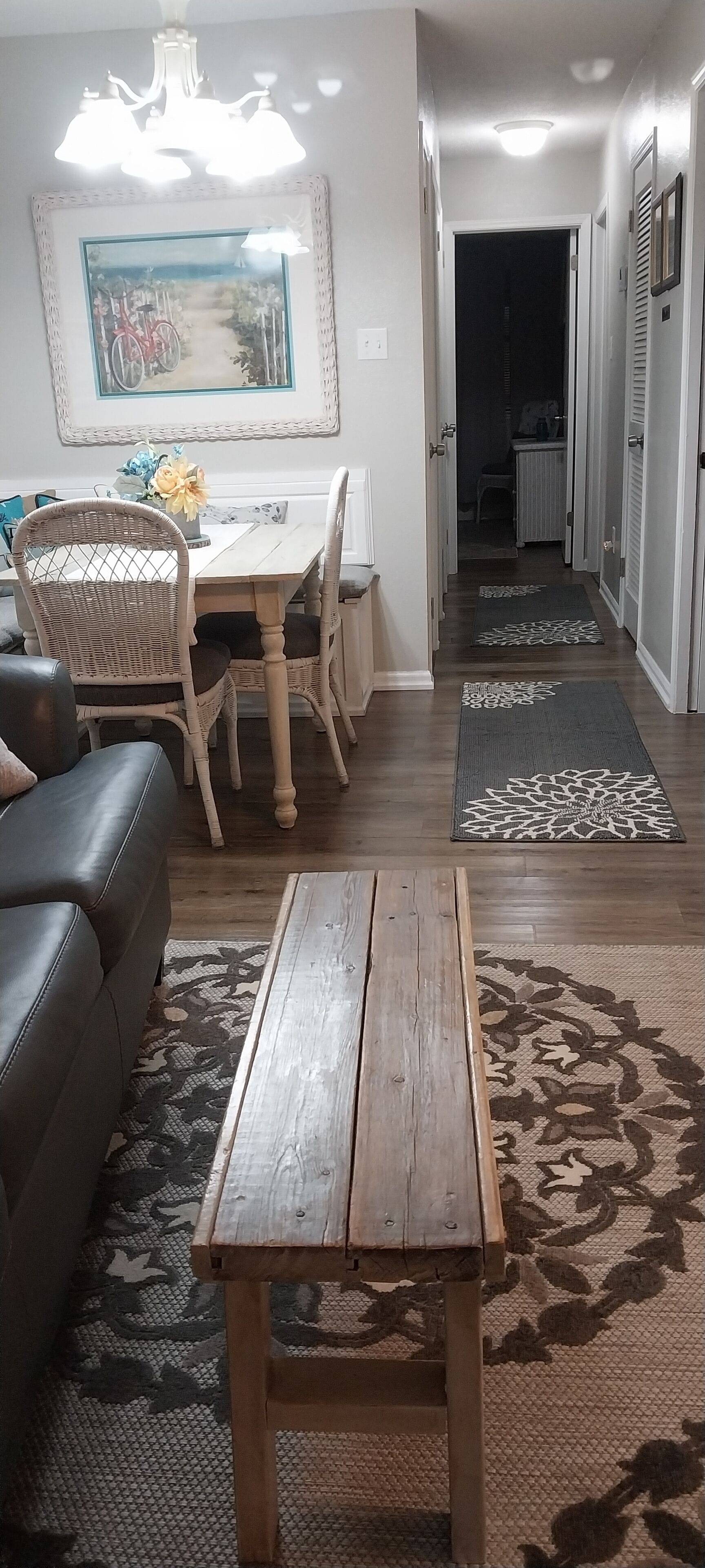 A living room with a wooden coffee table, a sofa, a dining table with chairs, and a painting on the wall.