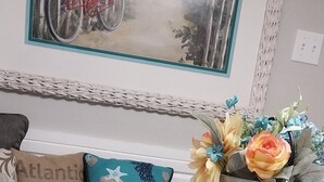 A white wooden table with a metal flower pot on a coaster, a wicker chair, and a cushion with a floral pattern.