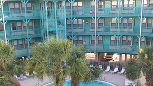A turquoise multi-story hotel with a swimming pool surrounded by palm trees and lounge chairs.