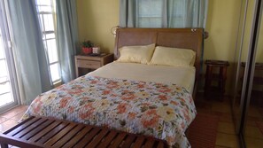 Een slaapkamer met een houten bed, een nachtkastje met een lamp, en een raam met gordijnen.