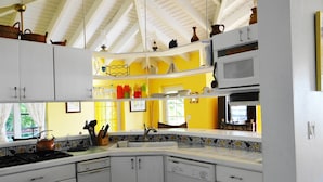 Una cucina con mobili bianchi, un forno a microonde e un lavello. Si vedono bottiglie colorate e una finestra con tende.
