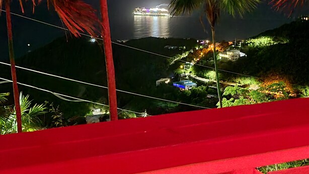 Una vista notturna di una zona costiera con edifici illuminati e una barca sull'acqua.