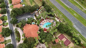 Vista aérea de una zona residencial con piscina, canchas de tenis y una carretera.