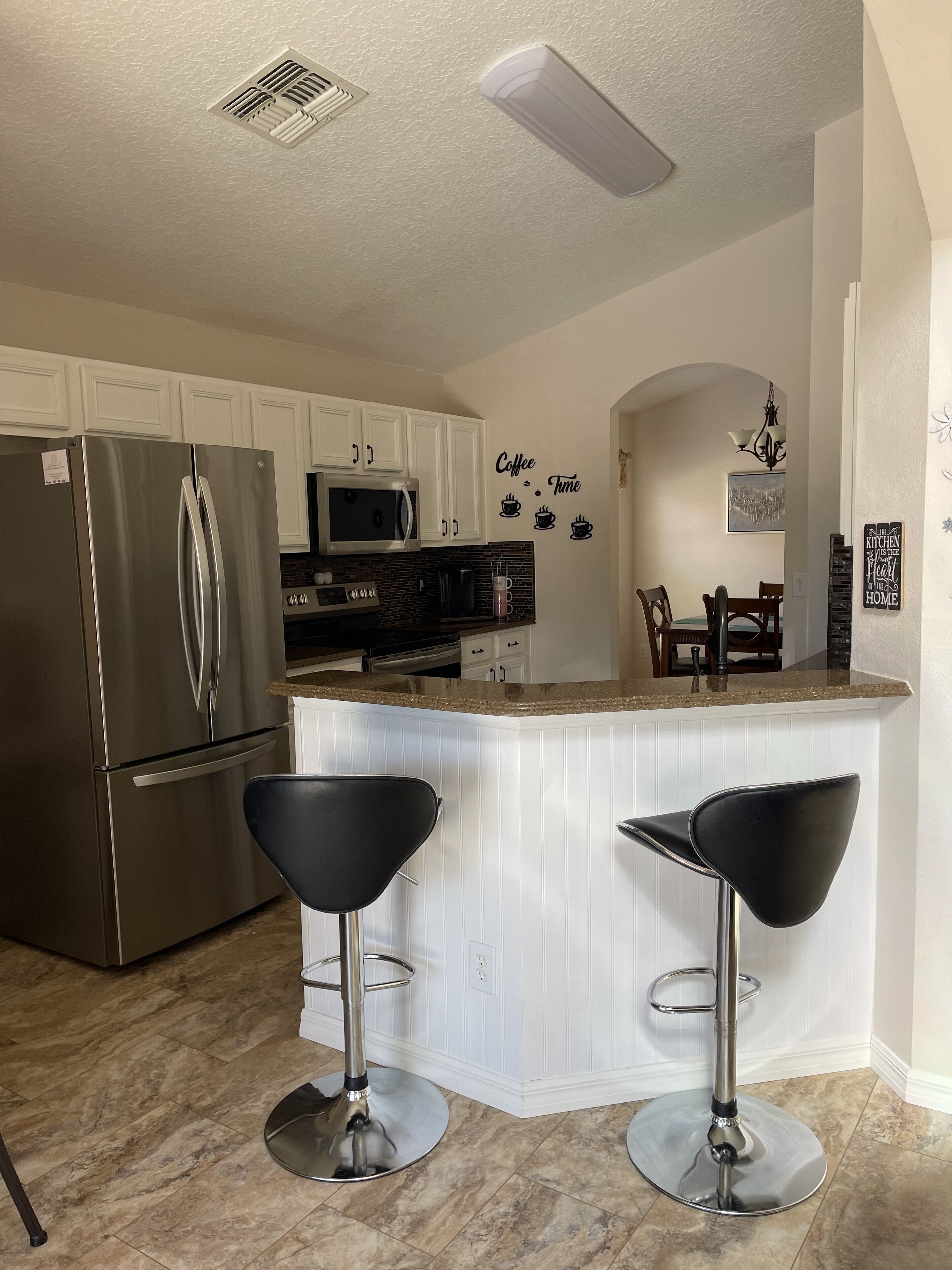 A modern kitchen with white cabinets, stainless steel appliances, and a central island with two black bar stools.