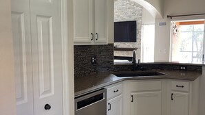 Una cocina con armarios blancos, salpicadero de ladrillo y lavavajillas integrado.
