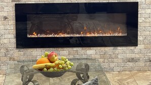 Una sala moderna con chimenea, una mesa de vidrio con frutero y una pared de ladrillo.