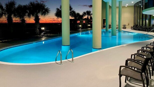 Une piscine intérieure avec vue sur le coucher de soleil, des palmiers et des chaises longues.