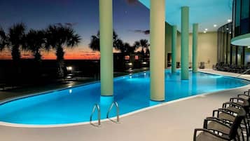 An indoor swimming pool with a sunset view, palm trees, and lounge chairs.
