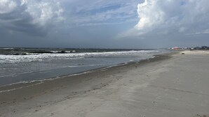 Une plage avec des vagues, un ciel dégagé et quelques personnes qui se promènent.