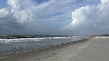 A beach with waves, a cloudy sky, and a distant building.
