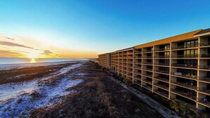 Un hotel de diseño moderno, con varios pisos y balcones, ubicado junto a una playa y vistas al atardecer sobre el océano.
