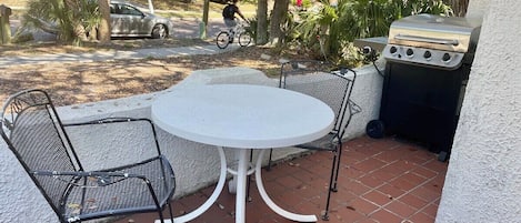 Une terrasse avec une table ronde et quatre chaises, un barbecue et un vélo garé à proximité.