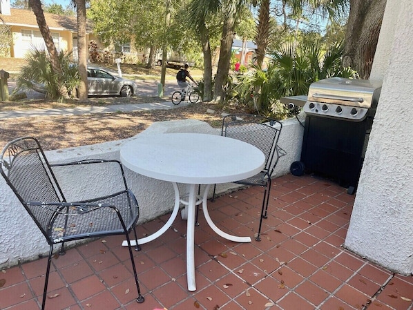 Un patio con una mesa redonda y cuatro sillas, una parrilla y una bicicleta estacionada cerca.