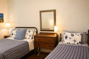 A bedroom with two single beds, a wooden dresser, a mirror, and a nightstand with a lamp.