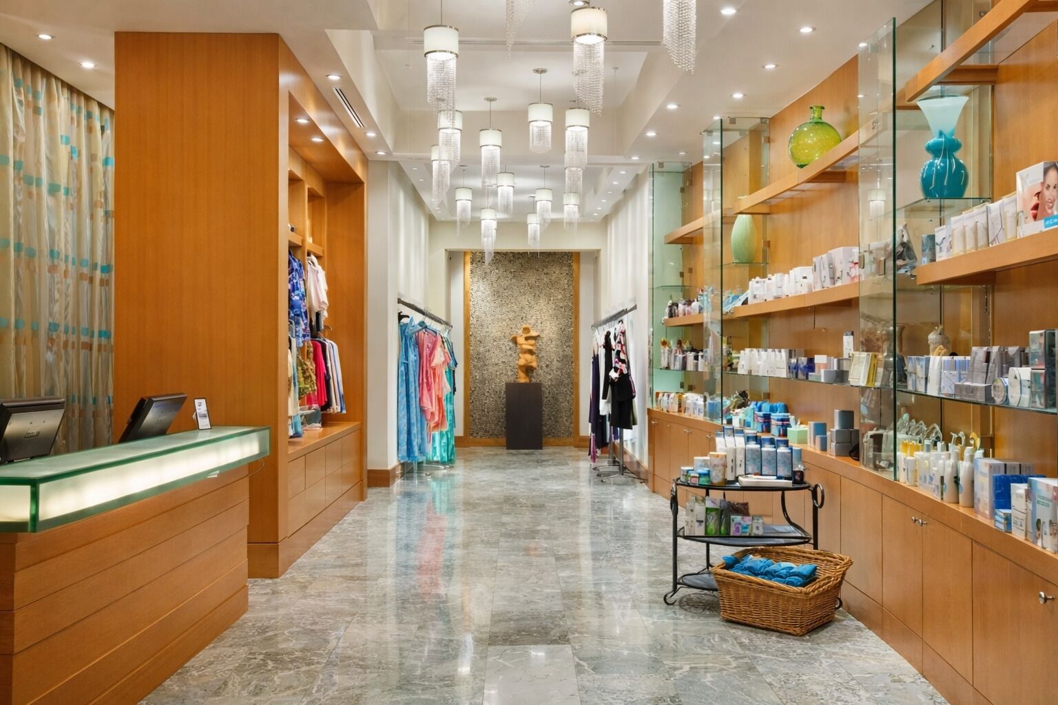 A hotel lobby with a reception desk, clothing racks, a statue, and shelves with toiletries.