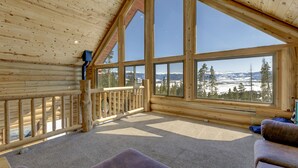 Een houten blokhut met een balkon, grote ramen en uitzicht op besneeuwde bergen.