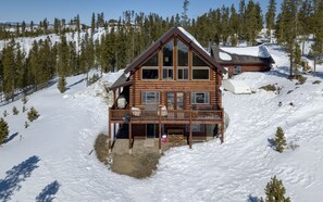 Una cabaña de troncos con balcón, rodeada de nieve y árboles.