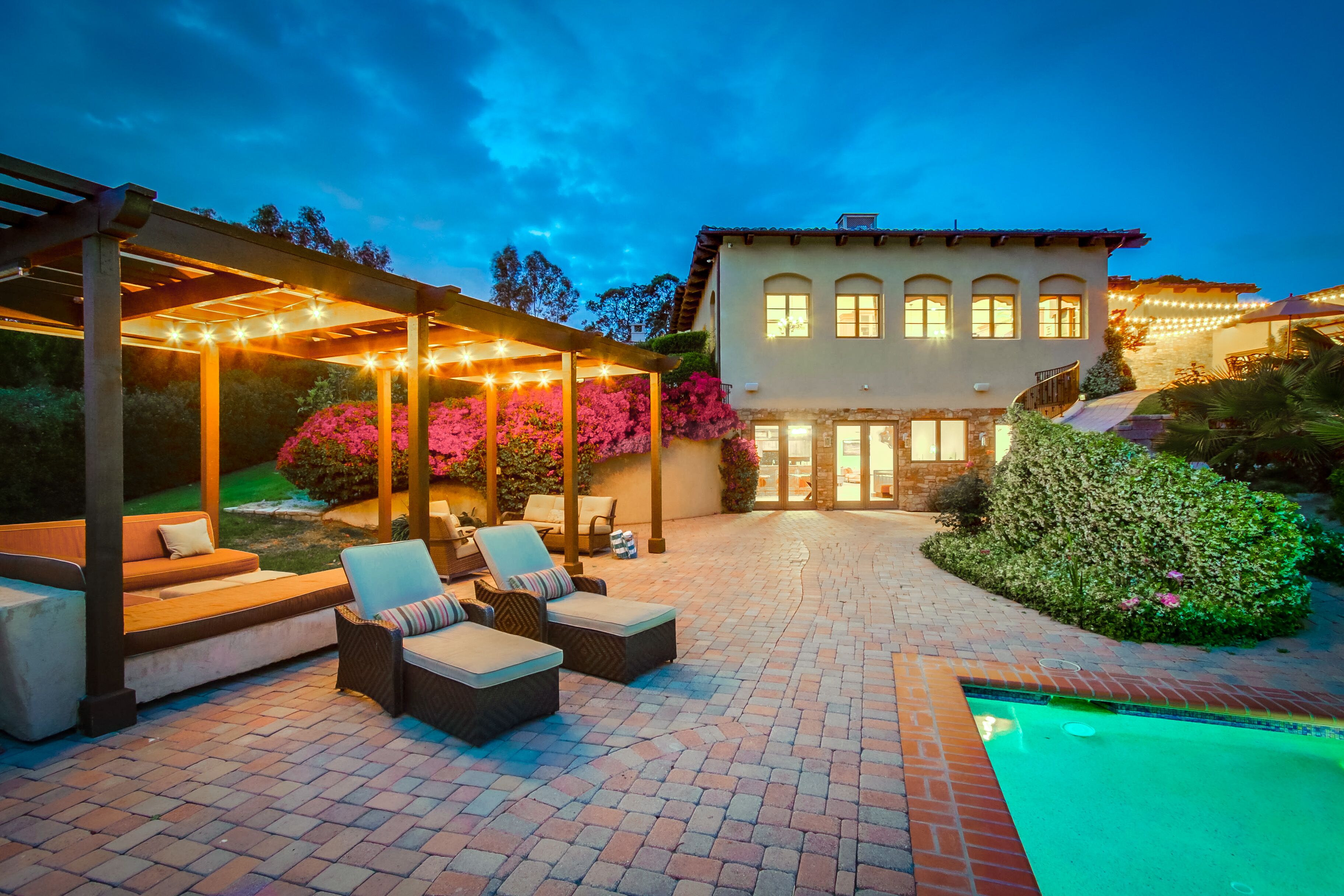 Un patio con mobiliario exterior, una piscina y una casa con numerosas ventanas.