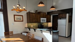 Ett kök med träskåp, en mikrovågsugn, ett kylskåp och ett matbord med stolar.