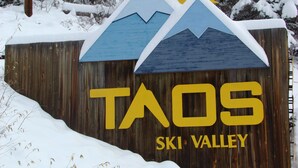 En träskylt med texten ”TAOS SKI VALLEY” och en illustration av ett berg och en sol.