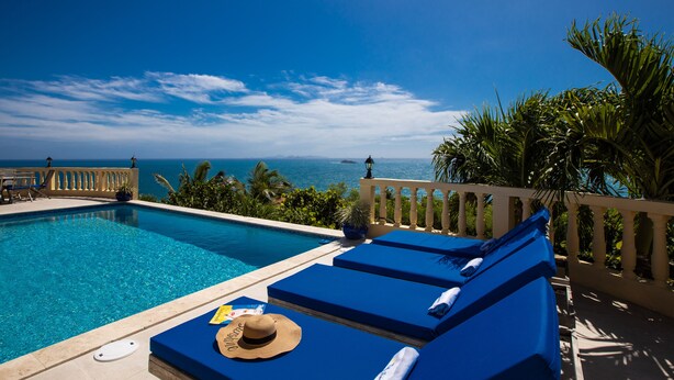 A poolside area with blue lounge chairs, a hat, and a towel.