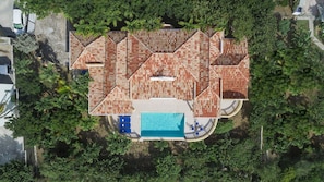 Eine Vogelperspektive zeigt ein Haus mit einem großen Schwimmbecken, umgeben von üppiger Vegetation.