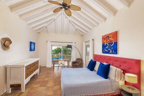 A bedroom with a bed, a desk, a chair, a ceiling fan, and a balcony with a view of palm trees. - Villa Tamarind - Luxury Oasis - Spectacular Views (Upper Prince's Quarter,)