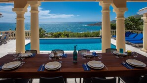A dining table set for six with a view of the ocean and a pool.