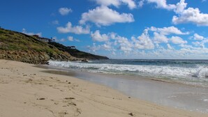 A beach with a rocky cliff and ocean waves.