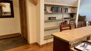 Uma cozinha com piso de madeira, bancada de granito e uma estante embutida com copos de vinho e livros.