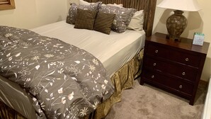 Cama bem arrumada com roupa de cama floral, cabeceira de madeira e mesa de cabeceira com abajur e caixa de lenços.