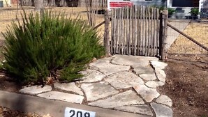 Ein Steinweg führt zu einem Holztor mit einem Schild, auf dem '208' steht.