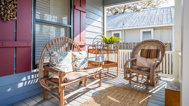 Eine Veranda mit Korbmöbeln, einem Blumentopf und einem Holenzaun.