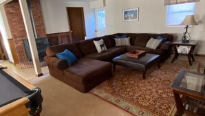 Ein Wohnzimmer mit Ecksofa, Couchtisch, gemustertem Teppich, Kamin und einer Tür zu einem anderen Raum.