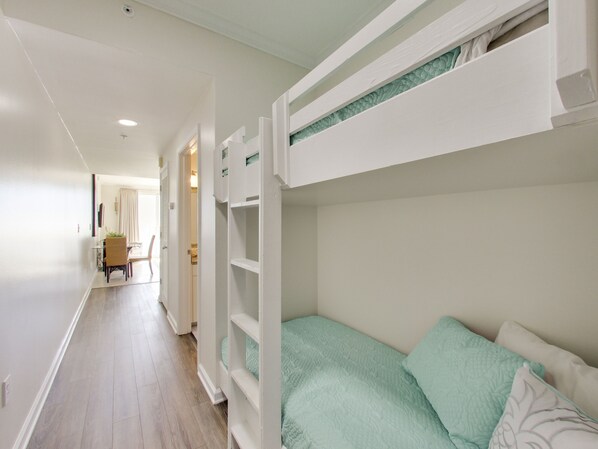 A bunk bed with a green bedspread, a white wall, and a wooden floor.