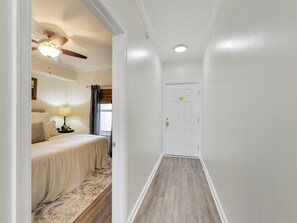 A narrow hallway with a white door at the end, a ceiling fan, and a lamp on a bedside table in a room. - Majestic Sun 909A. Beautiful Unit. Book today. Video Link! (Destin)