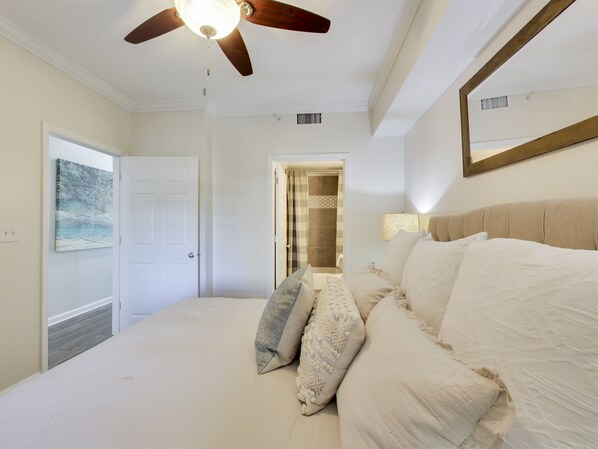 Une chambre à coucher avec un lit, des oreillers, un ventilateur de plafond, une porte et un tableau au mur.