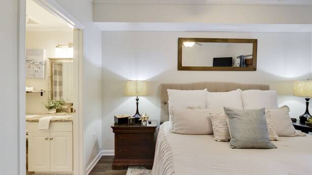 A bedroom with a bed, nightstands, a dresser, a mirror, and a door leading to a bathroom.